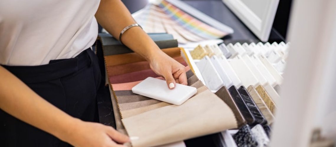 Asian woman interior designer chooses color of stone countertop for kitchen or facades compare with textile samples. Female professional indoor decorator working at showroom or residential apartment